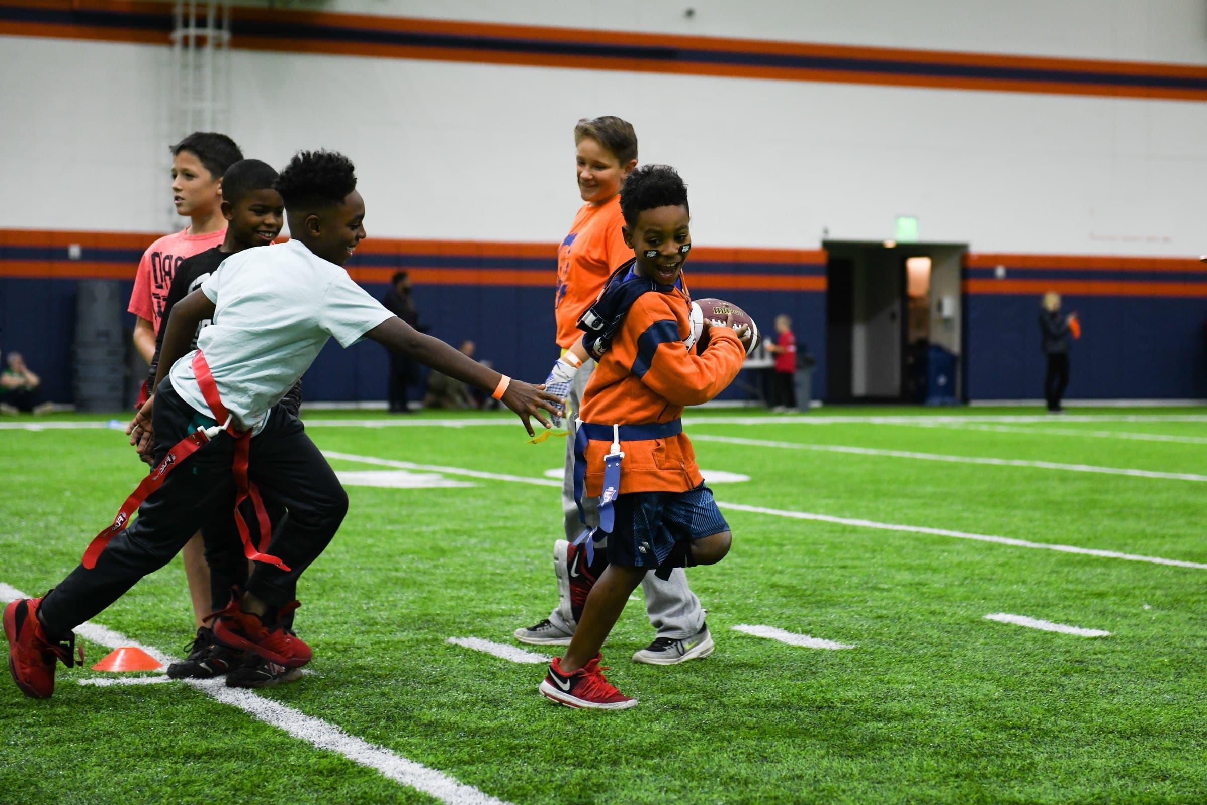 Kids playing flag football on an indoor turf field
